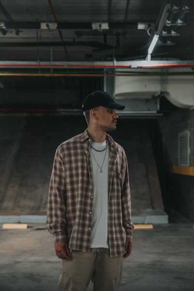 man in brown and white plaid dress shirt wearing black cap standing near train